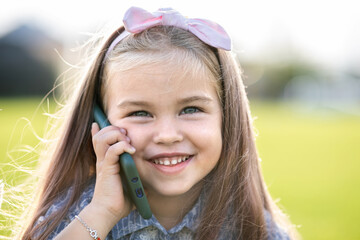 Pretty happy child girl talking on mobile phone smiling outdoors in summer.