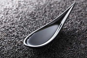 Sesame oil in small bowl on a background of black sesame.