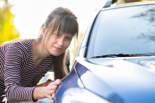 Young woman customer closely examining a new car at dealer outdoor shop before purchasing it.