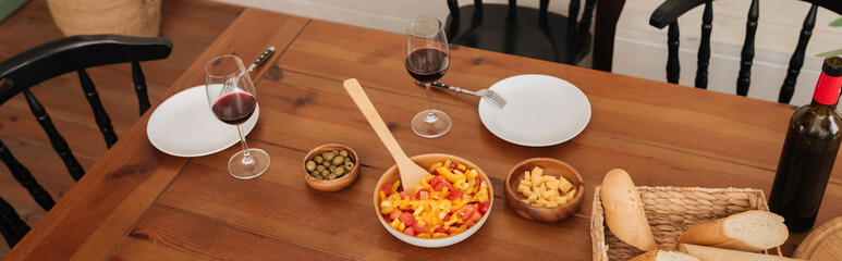 high angle view of served table with vegetarian dinner, wine glasses and baguette in kitchen, banner