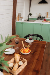 served table with vegetarian dinner and wine glasses in kitchen with blurred plant on foreground