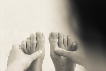 Horizontal black and white over the shoulder detail of yogini making forward bending exercise on the floor, reaching foot and touching toes with the hand. Indoor home yoga practice in sepia tone