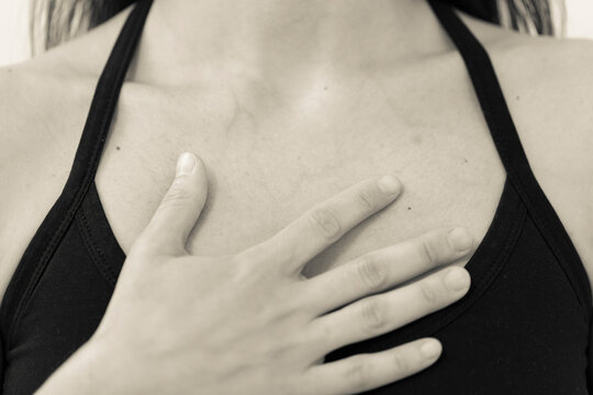BW horizontal detail of chest and shoulders of yogini wearing black one strap yoga top, with open hand placed on the heart area. Young adult woman meditating, feeling breath inhaling and exhaling