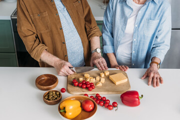 cropped view of elderly couple near chopping board with vegetables and cheese in kitchen