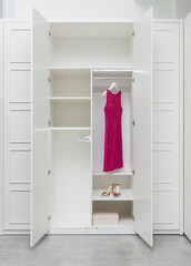 Pink dress and shoes in a white empty wardrobe as a part of a modern interior.