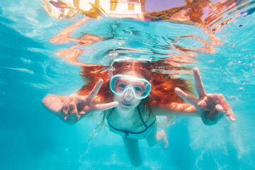 Obraz na płótnie Canvas Smiling happy portrait in scuba mask of the girl swim underwater in the pool and showing v victory gesture with hands