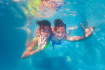 Obraz na płótnie Canvas Two happy teenage girls swim together hugging underwater in the pool waving hands