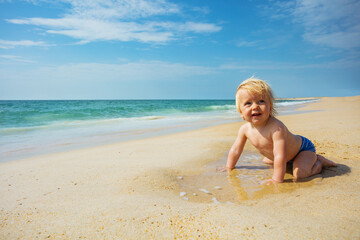 Fototapeta na wymiar Happy smiling little toddler crawl on the sand near the sea beach looking back