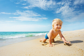 Fototapeta na wymiar Happy smiling little toddler crawl on the sand near the sea exploring the beach