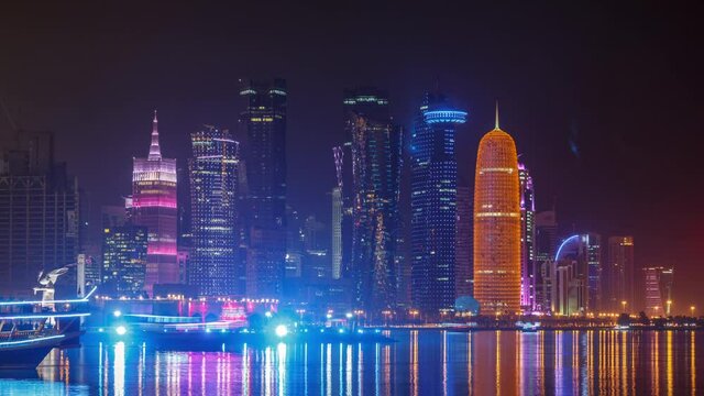 Traditional dhow boat in Doha at night timelapse, with modern buildings in the background. Illuminated skyscrapers on west bay from corniche