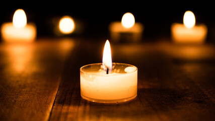 Burning candle light closeup in the dark. Beautiful bokeh and tealight atmosphere glowing at night background. Christian faith and hope concept - obrazy, fototapety, plakaty