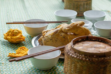 A traditionally cooked Vietnamese chicken dish surrounded by small bowls, chop sticks and a basket of freshly cooked rice