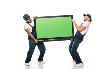 full length of multicultural movers carrying heavy plasma tv with green screen on white