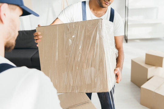 Indian Mover Holding Wrapped In Stretch Film Box Near Worker On Blurred Foreground