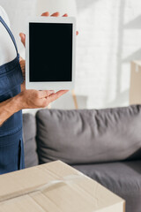 cropped view of mover in uniform holding digital tablet with blank screen in apartment