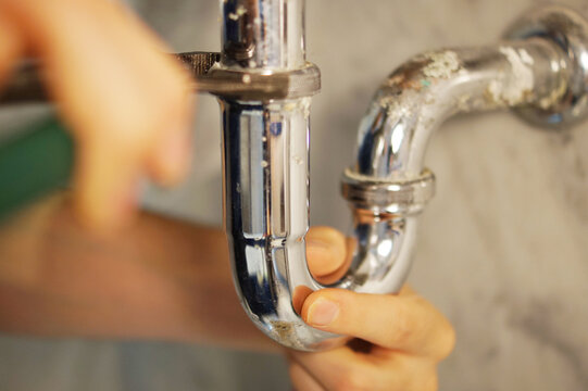 A close up of a hand holding a plumbing spanner screwing a fitting on wash basin waste pipe. 