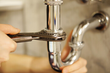 A close up of a hand holding a plumbing spanner screwing a fitting on wash basin waste pipe. 