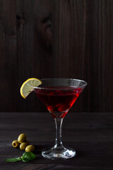 cosmopolitan cocktail in the bar. martini glass of red cocktail with olives and lemon with green mint on wooden background. Glasses for martini on the black table. copy space. alcohol drinks. vertical