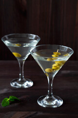 Two glasses margarita cocktail in the bar. martini glasses of cocktail with olives on wooden background. Glasses for martini and green mint on the black table. copy space. alcohol drinks.