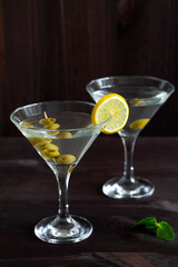 Two glasses margarita cocktail in the bar. martini glasses of cocktail with olives on wooden background. Glasses for martini with lemon and green mint on the black table. copy space. alcohol drinks.