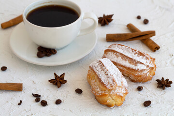 Vanilla eclairs on a plate on background. Coffee cup with coffee beans and anise star, cinnamon sticks on white table. copy space. Traditional french tasty dessert.