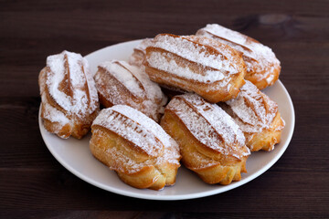 homemade vanilla eclairs or profiteroles on a white plate on a wooden table. copy space. Traditional french tasty dessert on dark table.