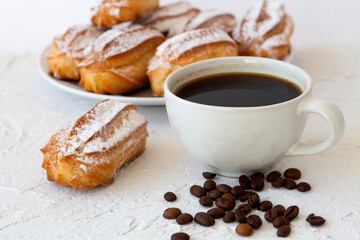 vanilla eclairs or profiteroles on a plate on a white table. copy space. Traditional french tasty dessert and coffee cup with coffee beans on white table.