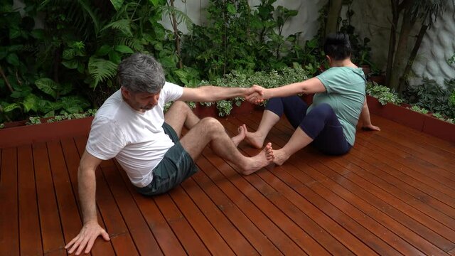 Pareja de mediana edad sentados en el jard&iacute;n de su casa mientras realizan estiramiento con ropa deportiva luego de entrenar  