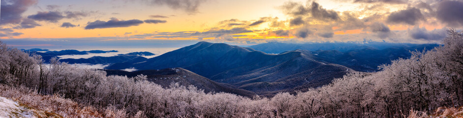 Devil's Knob Overlook – Panorama of Blue Ridge Mountains with low-level clouds, ice covered trees and plants, pink and yellow clouds at sunset