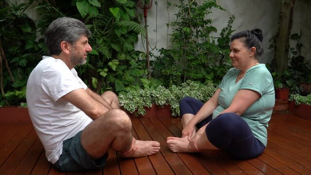 Pareja de mediana edad con ropa deportiva sentados en el jard&iacute;n de su casa realizando estiramiento luego de entrenar