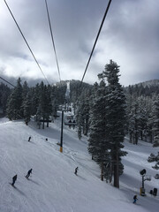 Moody winter scene at a ski resort on a grey and cloudy day, with a view of the chair lift, skiers and snow covered trees