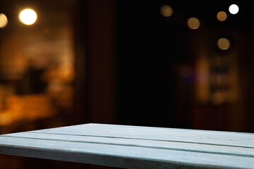 empty wooden table on blurred light gold bokeh of cafe restaurant on dark background, blurred cafe interior place for your products on the table