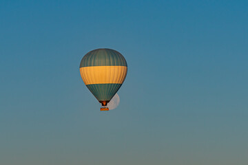 Fototapeta premium Hot air balloon flying over Cappadocia with full moon, blue sky