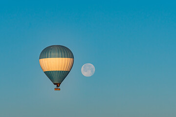 Hot air balloon flying over Cappadocia with full moon, blue sky