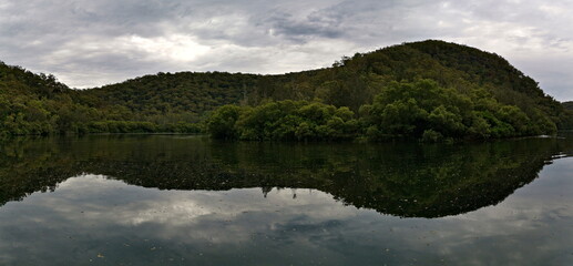 Beautiful panoramic view of a creek with reflections of mountains, trees, and cloudy sky on water, Crosslands Reserve, Berowra Valley National Park, New South Wales, Australia
