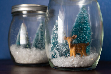 Glass jar winter scene with pine trees, snow, and deer