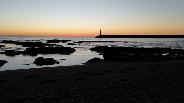 Beach sunset with two silhouettes walking torwards a beacon