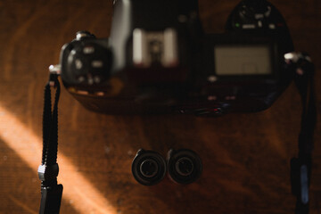 Two rolls of film sitting next to a black film camera on wooden background, seen from above, looking down