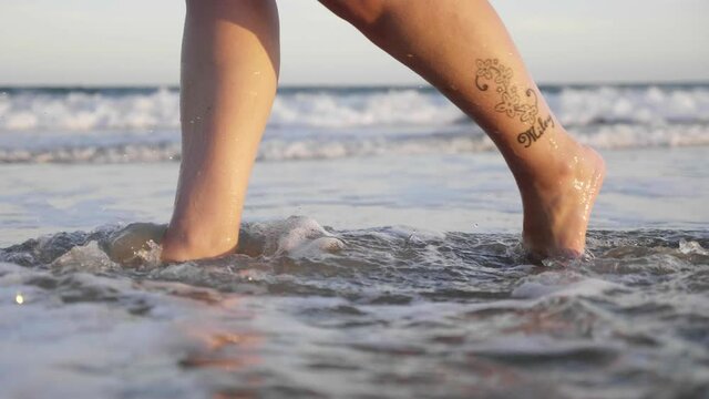 Woman Feet Walking on the Shore Splashing Through the Water, Close-up Slow Motion.