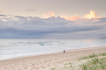 Fototapeta na wymiar Person sitting on the beach watching the sun rise.