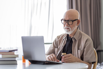 senior businessman working on laptop while hold on a bottle of medicine.