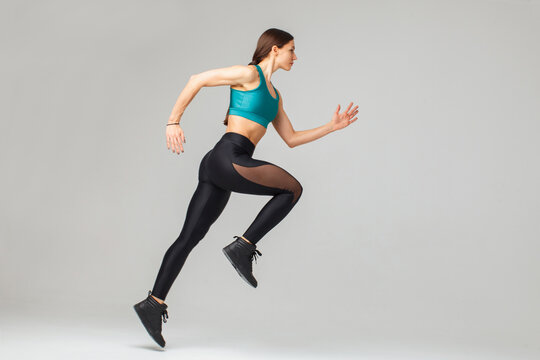 muscular athletic woman running isolated on gray background, side view
