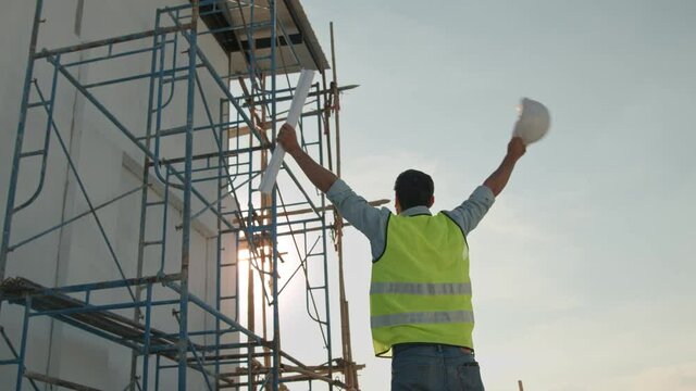 Engineer take of helmet and holding blueprint waving hand on rooftop of  building construction site 