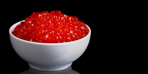 Red caviar in a white cup on a black background with a reflection.