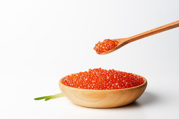 Red caviar in a wooden cup on a white background with a spoon.