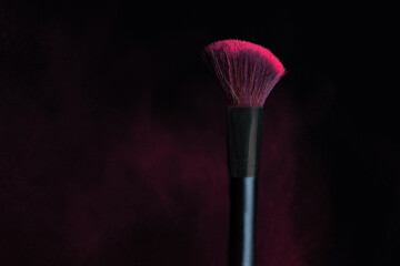 Make-up brush with pink powder explosion isolated on a black background