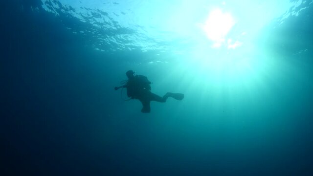 scuba diver photographer underwater taking photos blue ocean scenery of scubadiver silhouette sun beams and rays 