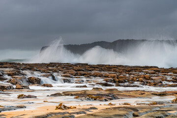 Rock platform, cascades and splashes with rain clouds by the seaside