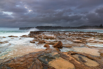 Fototapeta na wymiar Rock platform, cascades and splashes with rain clouds by the seaside