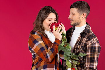 Handsome couple on a red background. The man gave the girl a bouquet of red roses. Holiday concept.